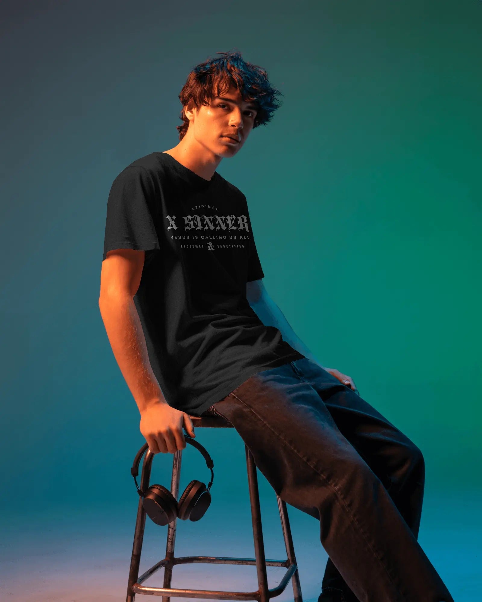 Person sitting on a stool with headphones, wearing a black t-shirt with text, against a gradient blue background.